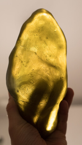 Auf der Fotografie ist ein gelbes Glasobjekt zu sehen mit nichtglatter Oberfläche. Eine Hand hält dieses Objekt. Die Finger scheinen von hinten durch. Der Daumen steht im Vordergrund. Das Bild vermittelt den Eindruck einer flamme die leuchtet und nach oben gehalten wird. 