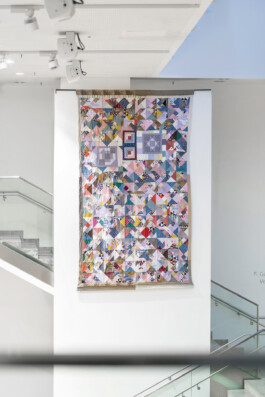Fotografie, die die hochformatige Patchworkarbeit zeigt, wie sie an einer Wand hängt.